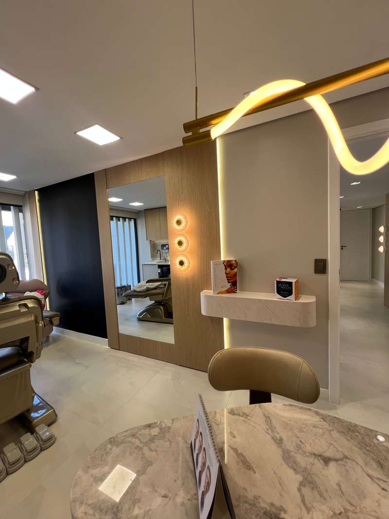 Consultório com cadeira odontológica, espelho na parede e uma luminária em linha contínua