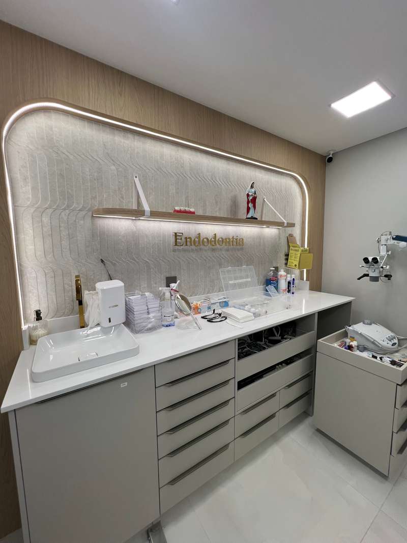 Consultório de endodontia com bancada branca, nicho iluminado com a palavra Endodontia e microscópio ao lado
